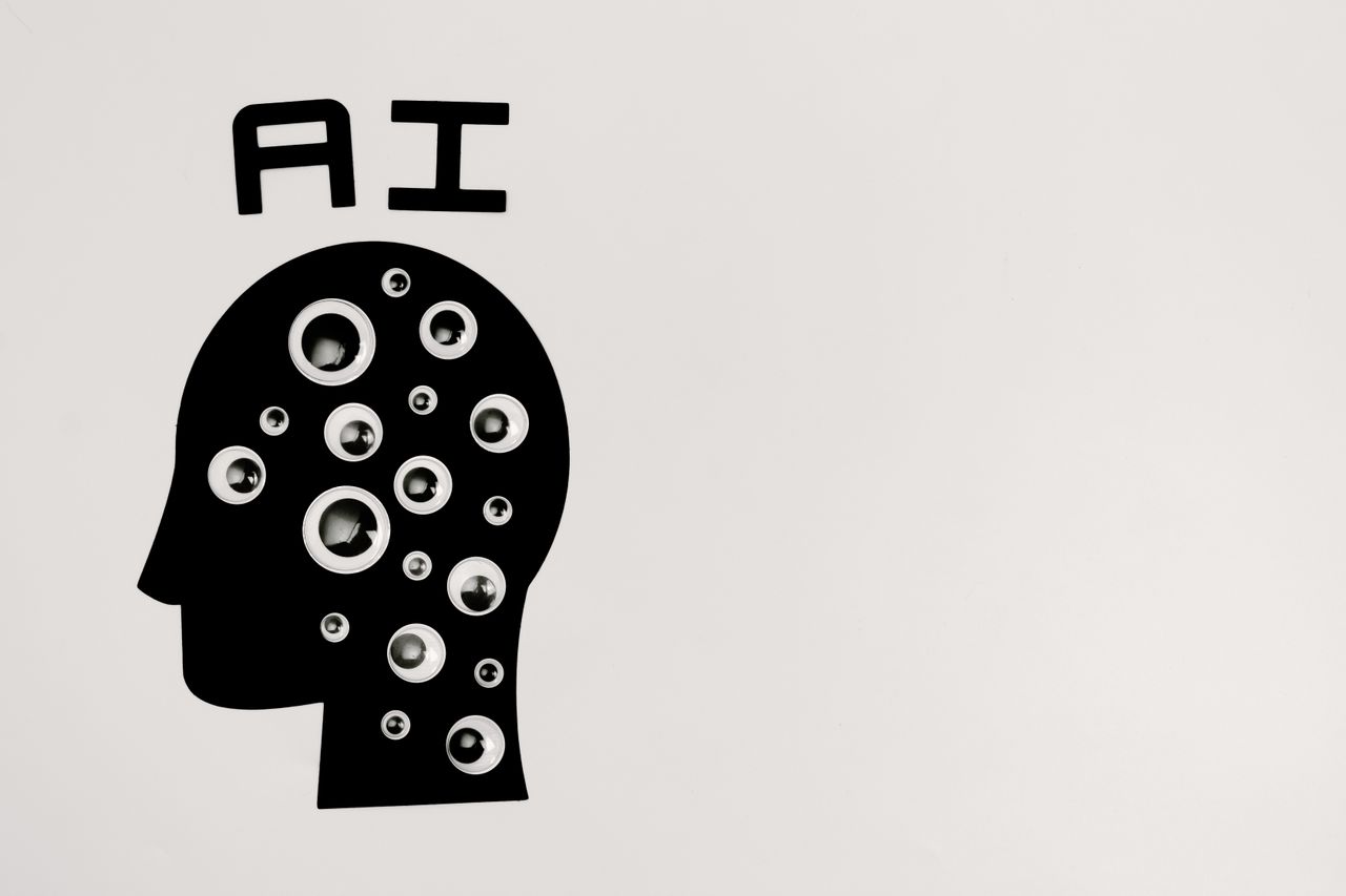 Een zwart silhouet van een hoofd met de letters AI erboven, gevuld met kijkende oogjes; een conceptbeeld over de grenzen van kunstmatige intelligentie